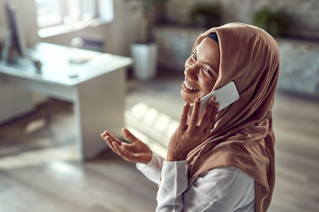 Gelukkige islamitische zakenvrouw die telefoneert terwijl ze op kantoor werkt