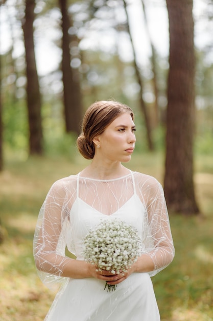 Gelukkige jonge bruid in een dennenbos witte trouwjurk