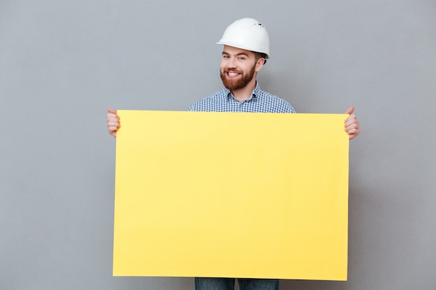 Gratis foto gelukkige jonge gebaarde bouwer die lege raad houden