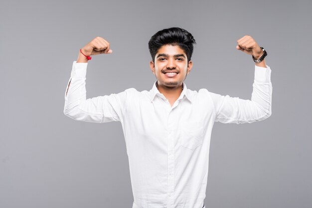 Gelukkige jonge Indische mens die bicepsen over grijze muur toont