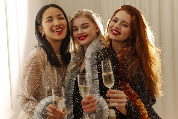 Gelukkige jonge interraciale vriendinnen in feestoutfits die champagne drinken terwijl ze afstuderen vakantieconcept vieren