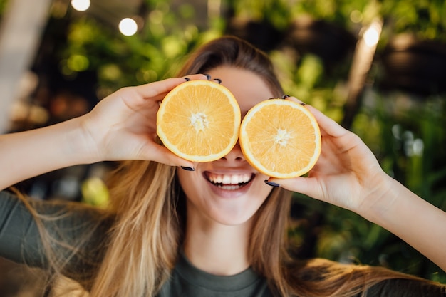 Gratis foto gelukkige jonge kaukasische vrouw die verse sinaasappelen voor ogen houdt en glimlacht