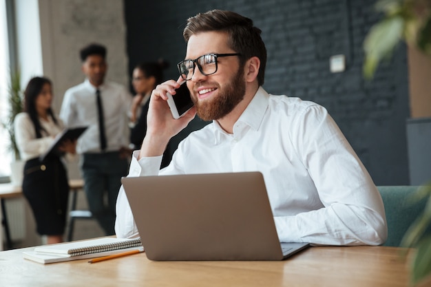 Gelukkige jonge Kaukasische zakenman die door mobiele telefoon spreekt.