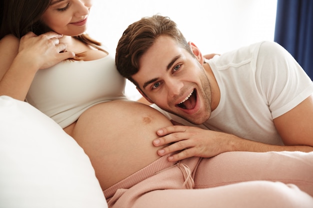 Gelukkige jonge man die de buik van zijn zwangere vrouw luistert