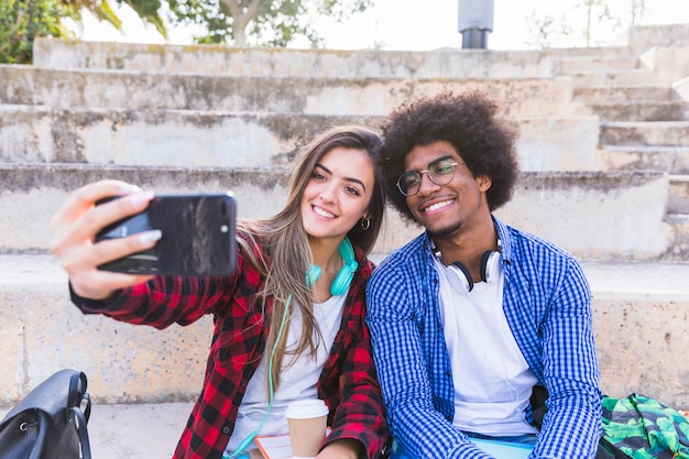 Gelukkige jonge mannelijke en vrouwelijke student die selfie op mobiele telefoon in openlucht nemen