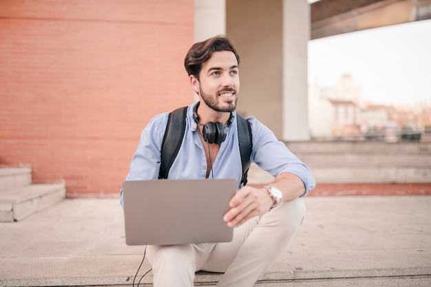 Gelukkige jonge mens die laptop met behulp van