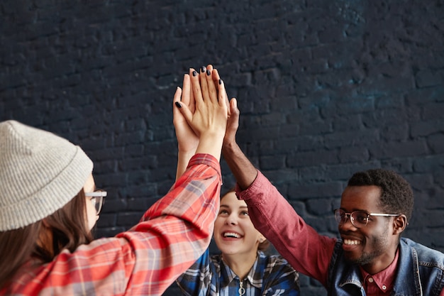Gelukkige jonge mensen die high five geven die elkaar meppen dienen gelukwens in tijdens vergadering bij koffie. creatieve ondernemers in informele kleding lachen en vieren het succes van een start-up project