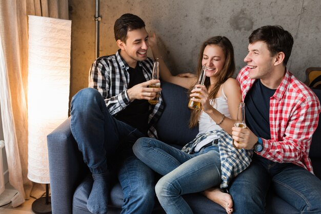 Gelukkige jonge mensen zittend op de bank, bier drinken, handen close-up roosteren, plezier maken, homeparty vrienden, hipster gezelschap samen, twee mannen één vrouw, glimlachen, positief, ontspannen, rondhangen, lachen