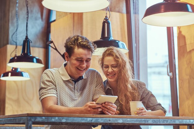 Gelukkige jonge paar studenten met behulp van een digitale tablet zittend aan een tafel in de kantine van de universiteit tijdens een pauze.