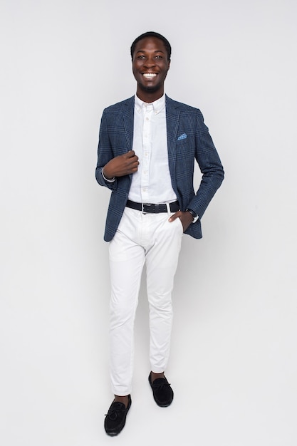 Gratis foto gelukkige jonge succesvolle man in stijlvolle zakelijke kleding die op een geïsoleerde witte muur staat