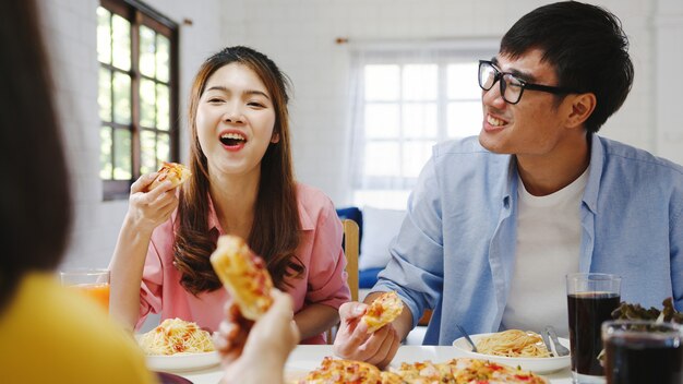 Gelukkige jonge vriendengroep die thuis lunch heeft. Azië familiefeest pizza eten en lachen genieten van maaltijd zittend aan de eettafel samen thuis. Viering vakantie en saamhorigheid.