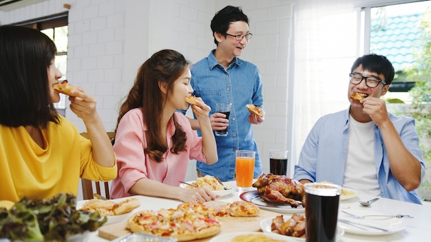 Gelukkige jonge vriendengroep die thuis lunch heeft. Azië familiefeest pizza eten en lachen genieten van maaltijd zittend aan de eettafel samen thuis. Viering vakantie en saamhorigheid.