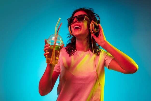 Gelukkige jonge vrouw die aan de muziek luistert en over trendy blauwe neon glimlacht