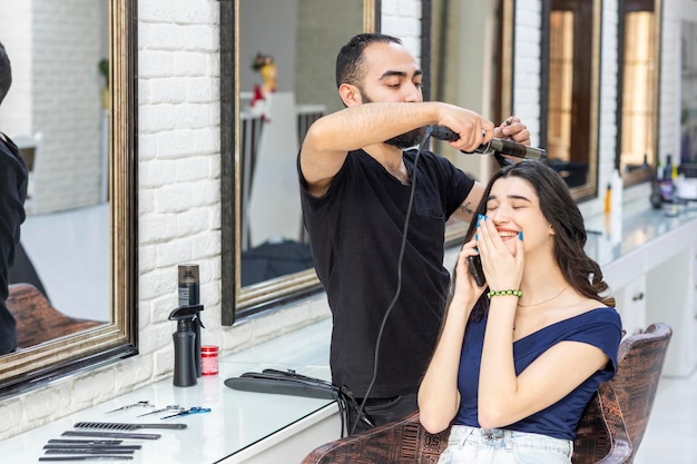 Gelukkige jonge vrouw die bij de kapper zit en kapper haar haar vormgeeft Foto van hoge kwaliteit