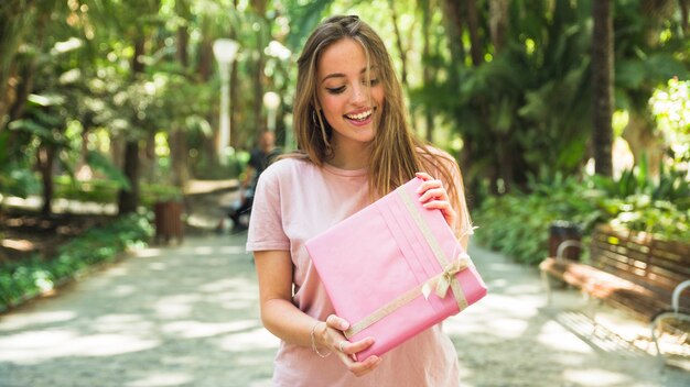 Gelukkige jonge vrouw die roze giftdoos in park houdt