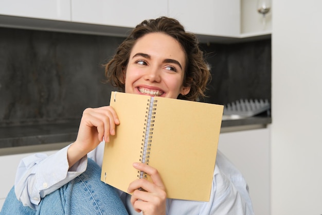 Gelukkige jonge vrouw die thuis studeert, een dagboek leest, zich voorbereidt op een examen en naar haar aantekeningen in het notitieboek kijkt