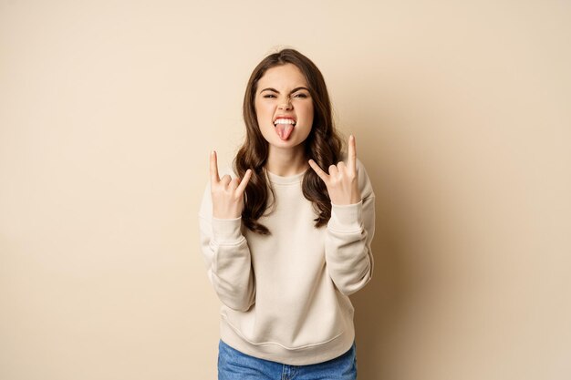 Gelukkige jonge vrouw die van muziek geniet die pret heeft die rots op heavy metal vingerhoorns gebaar staand toont...