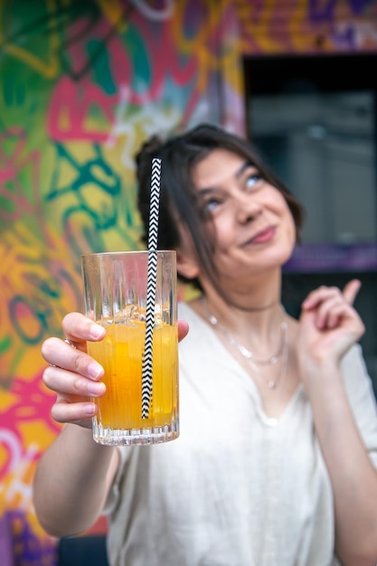 Gelukkige jonge vrouw met een glas limonade tegen een fel geschilderde muur