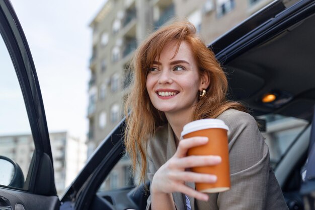 Gelukkige jonge vrouw met koffie die een rem in haar auto heeft Zijaanzicht van vrouw met koffie om in de hand te gaan Jonge vrouw die koffie drinkt in haar auto