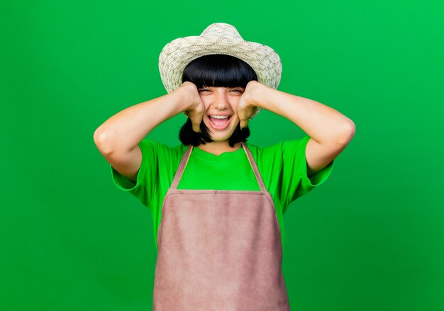 Gelukkige jonge vrouwelijke tuinman in uniform met een tuinhoed houdt het hoofd geïsoleerd