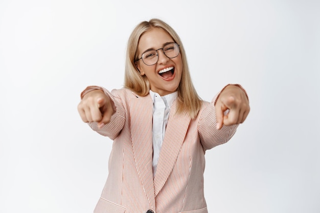 Gelukkige jonge zakenvrouw die met de vingers naar de camera wijst en je feliciteert terwijl je op een witte achtergrond staat