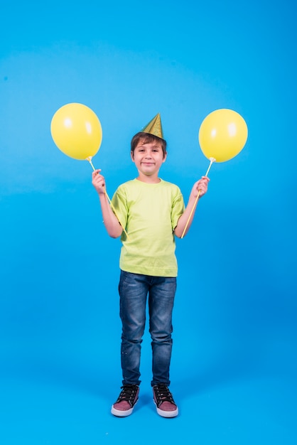 Gelukkige jongen die de holdingsballons van de partijhoed op blauwe achtergrond draagt