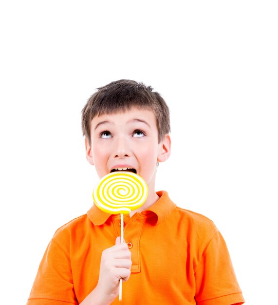 Gelukkige jongen die in oranje t-shirt gekleurd suikergoed eet - dat op wit wordt geïsoleerd