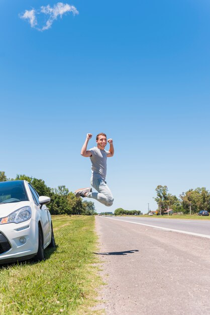 Gelukkige jongen die op de weg naast auto springt