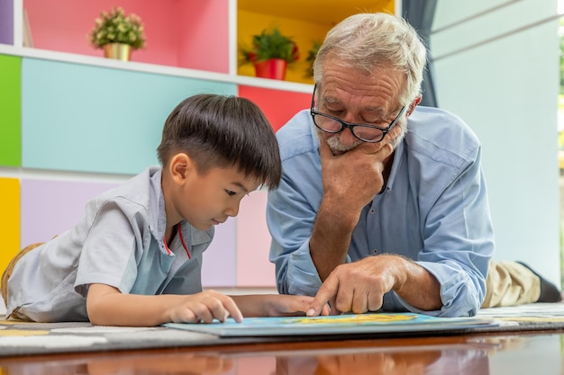 Gratis foto gelukkige jongen kleinzoon leesboek met oude senior man grootvader thuis