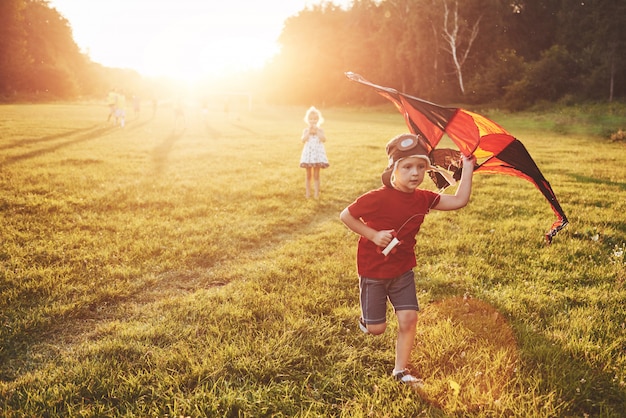 Gelukkige kinderen lanceren een vlieger in het veld bij zonsondergang. Kleine jongen en meisje op zomervakantie