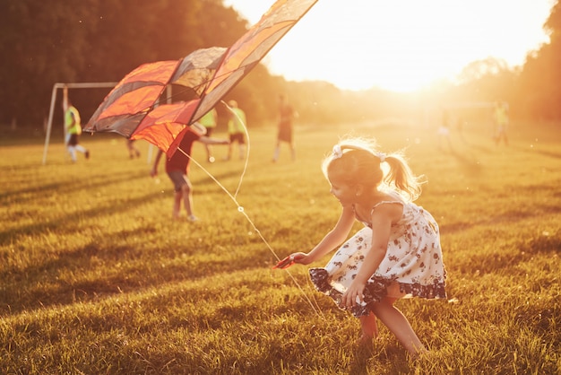 Gelukkige kinderen lanceren een vlieger in het veld bij zonsondergang. Kleine jongen en meisje op zomervakantie