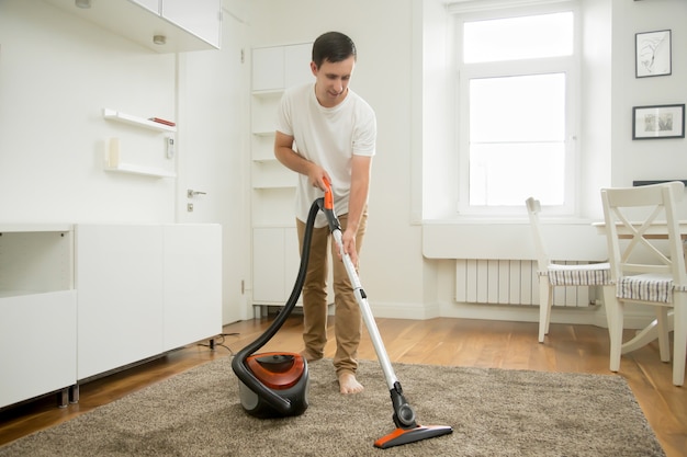 Gelukkige lachende man die het tapijt schoonmaakt