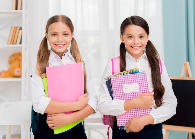 Gratis foto gelukkige leuke schoolmeisjes die met voorbeeldenboeken glimlachen