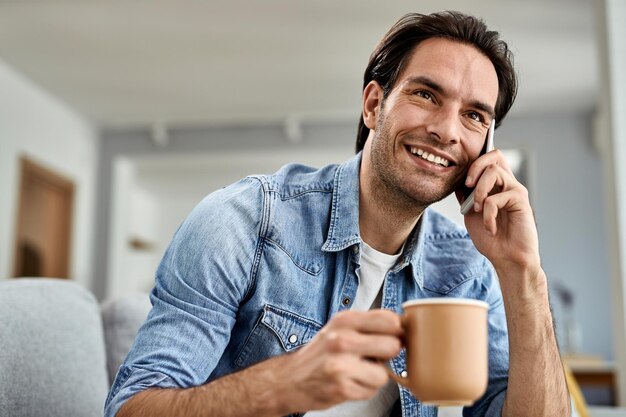 Gelukkige man die koffie drinkt en thuis communiceert via mobiele telefoon