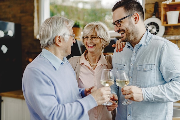 Gelukkige man die wijn drinkt en met zijn oudere ouders praat terwijl hij ze thuis bezoekt