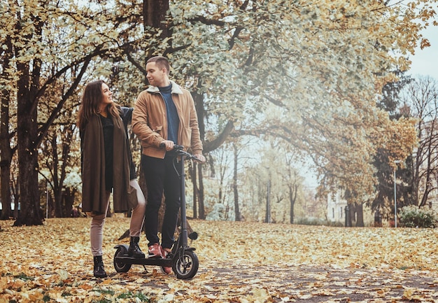 Gelukkige man en vrouw hebben een mooie rit op de scooter in het gouden herfstpark.