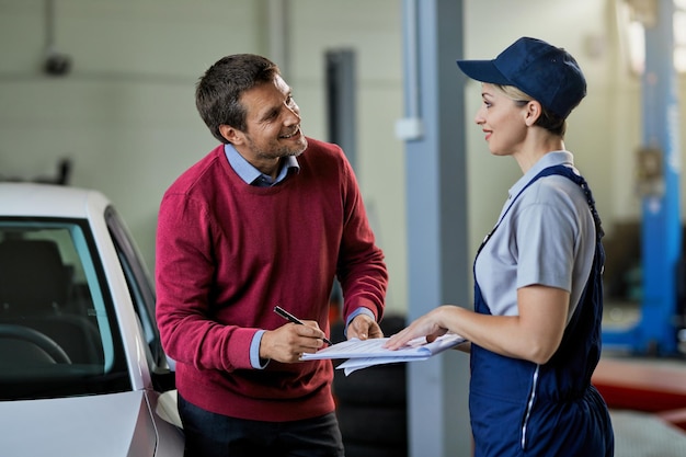 Gelukkige man praat met vrouwelijke monteur terwijl hij papierwerk ondertekent in autoreparatiewerkplaats