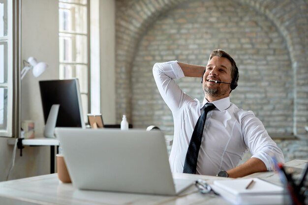 Gelukkige mannelijke ondernemer ontspannen op kantoor na een online vergadering via een computer