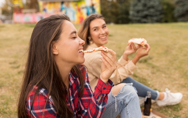 Gelukkige meisjes die pizza buiten eten