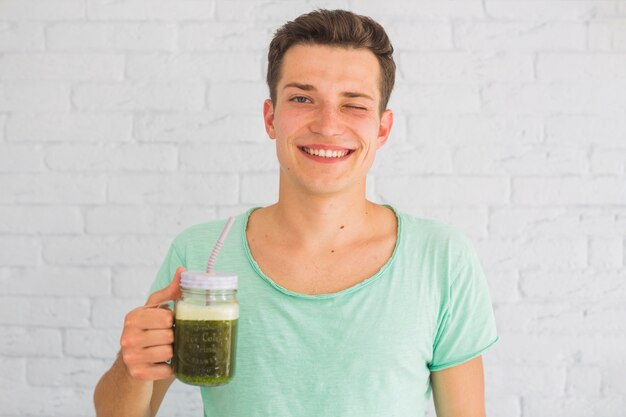 Gelukkige mens die gemengde groene smoothies in kruik het knipogen houden