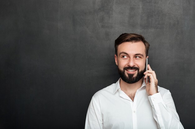 Gelukkige mens die op mobiele telefoon spreekt die prettig gesprek heeft dat opzij over grafietexemplaarruimte kijkt