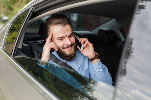 Gelukkige mensenzitting binnen auto die op smartphone spreken