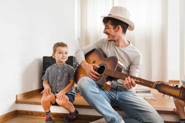 Gelukkige mensenzitting met zijn zoon het spelen gitaar