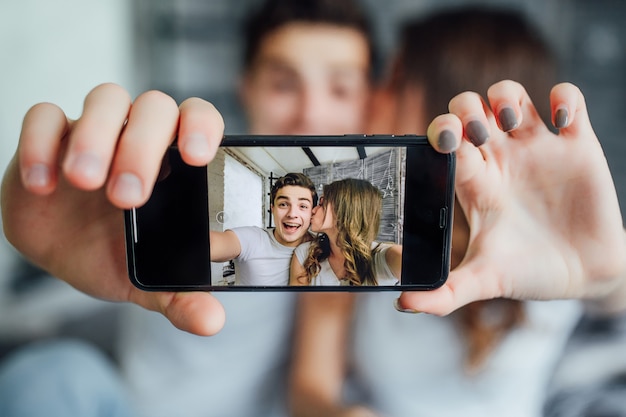 Gelukkige minnaar die de technologiesmartphone gebruikt voor selfie op het bed in de slaapkamer thuis