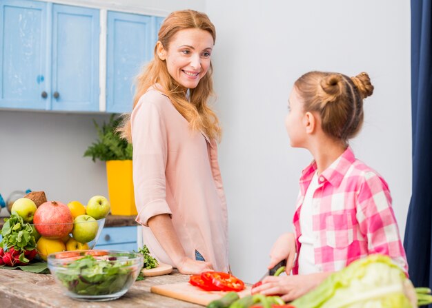 Gelukkige moeder die haar dochter bekijkt die de salade in de keuken voorbereidt