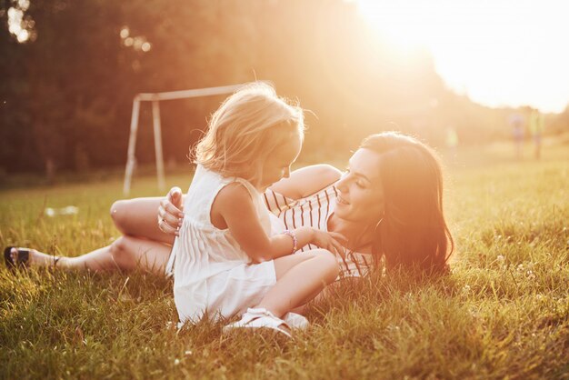 Gelukkige moeder en dochter knuffelen in een park in de zon op een heldere zomer van kruiden.