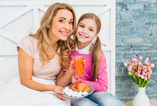 Gratis foto gelukkige moeder en dochterzitting met croissant op bed