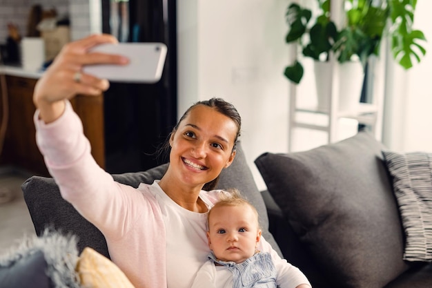 Gelukkige moeder en haar baby nemen selfie met smartphone in de woonkamer