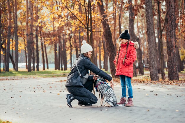 Gelukkige moeder en haar dochter spelen met hond in herfst park