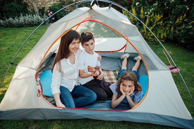 Gelukkige moeder met haar dochter en zoon in tent op gras bij park